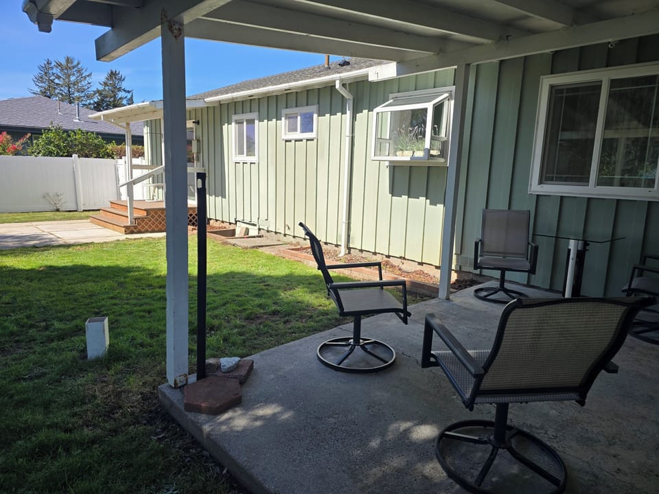 Shaded patio with swivel seating, lawn, and private fenced yard