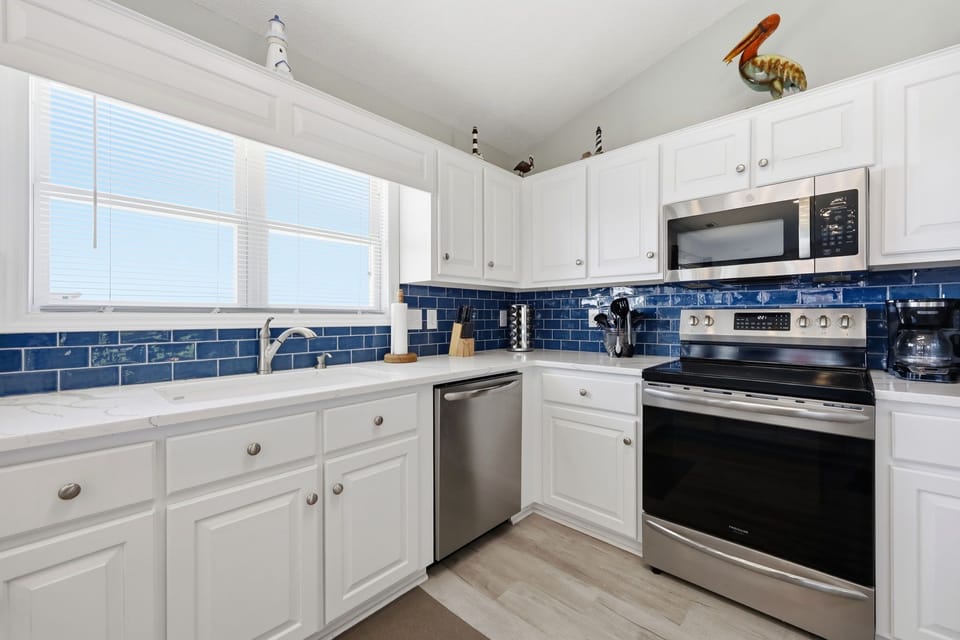 This bright, coastal-inspired kitchen features crisp white cabinetry, gleaming stainless steel appliances, and charming blue subway tile backsplash that brings the beach home with you.