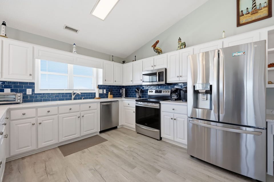 Your spacious kitchen features crisp white cabinetry, stainless steel appliances, and a bright blue tile backsplash that adds a coastal charm. Natural light from skylights makes meal prep a joy.