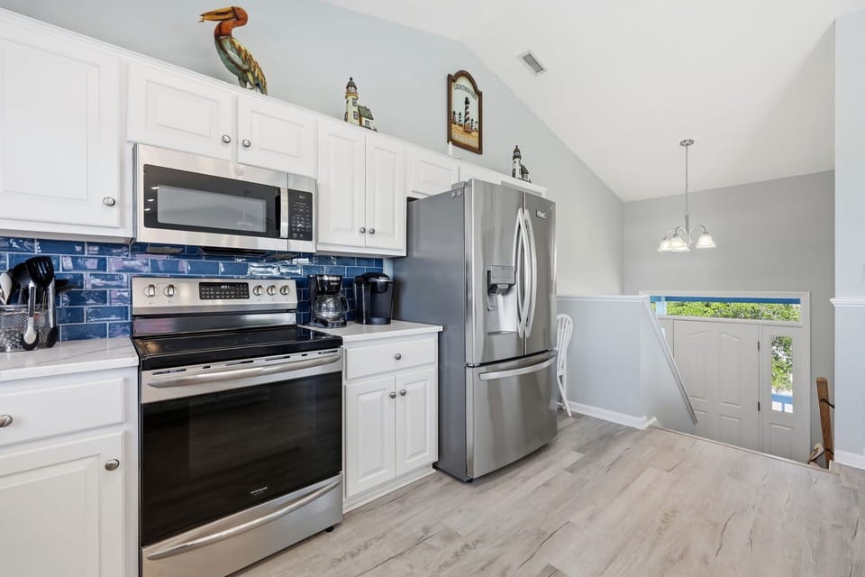 Step into your fully equipped kitchen where cooking becomes a pleasure. Crisp white cabinetry, modern stainless steel appliances, and a charming blue tile backsplash create a bright, welcoming space for preparing your favorite vacation meals.