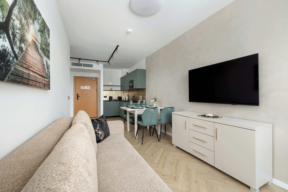 A living space with a wall-mounted TV and a beige sofa. Light wood flooring enhances the brightness of the room. The layout feels clean and modern.