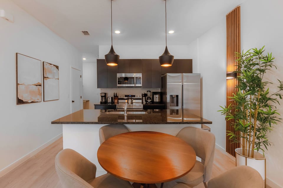 Welcome to this delightful kitchen, where dark cabinetry contrasts with light walls for a warm ambiance. Enjoy cozy meals at the round dining table, enhanced by modern pendant lights and surrounded by fresh greenery.