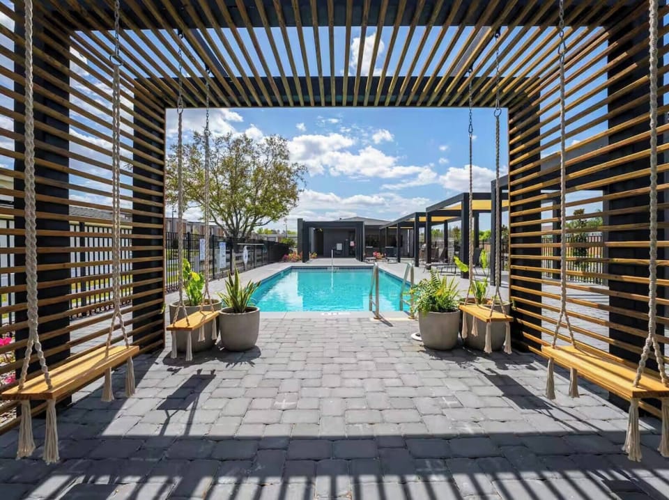 Step into a tranquil outdoor lounge framed by stylish wooden slats, where plush seating invites relaxation beside a shimmering pool. Lush greenery enhances the atmosphere, making it an ideal spot to unwind and enjoy the sun.