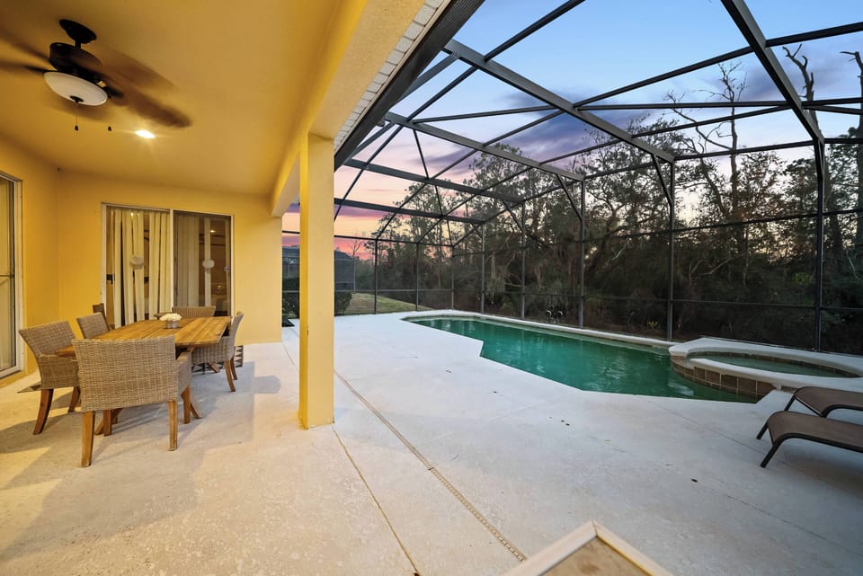 Step outside to your private oasis, where a shimmering pool awaits under a spacious screened enclosure. Enjoy al fresco dining at the stylish table, surrounded by tranquil greenery and the warm hues of the evening sky.