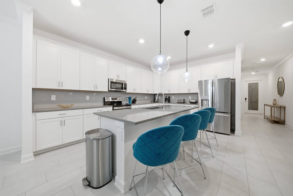 Welcome to this bright kitchen with sleek white cabinetry and a spacious island adorned with striking turquoise bar stools. Modern appliances and polished countertops create a stylish atmosphere for meal prep or casual gatherings.