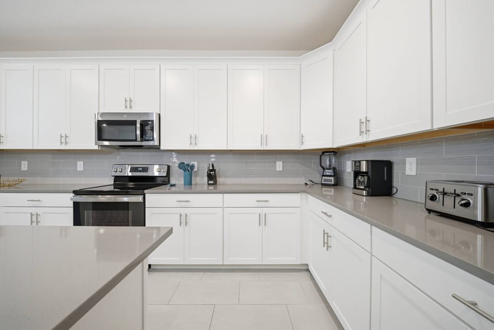 Welcome to a bright, functional kitchen featuring sleek white cabinetry and polished gray countertops. With modern appliances like a stainless steel microwave and coffee maker, it's the ideal space to inspire your culinary.