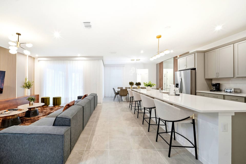Welcome to a stylish open-concept living area with a sleek gray sofa perfect for relaxation, bathed in natural light from large windows. The modern kitchen boasts elegant bar seating, warm wood accents, and contemporary lighting.