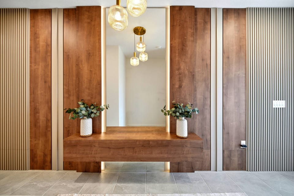 Welcome to a stunning entryway featuring rich wood paneling and warm tones. Chic lighting casts a gentle glow on the elegant console table, adorned with fresh greenery to create a delightful first impression for our guests.