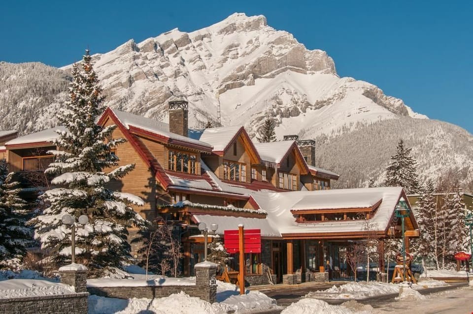 Snow-covered peaks rise behind the inn's timber exterior — this is Banff Avenue in winter