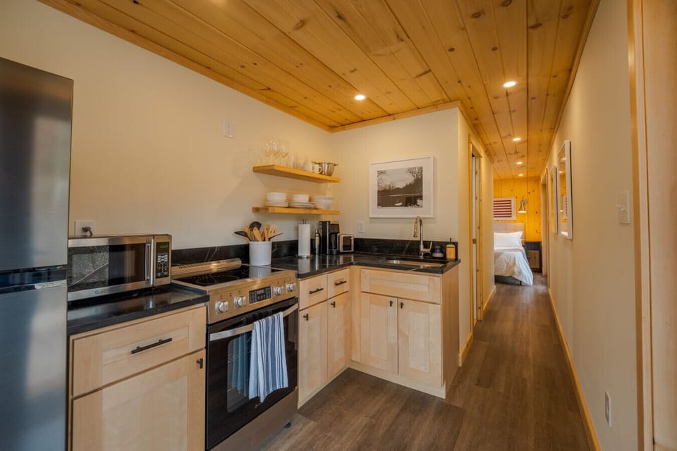 Fully equipped modern kitchen with stainless steel appliances, open shelving, and a seamless flow into the living space