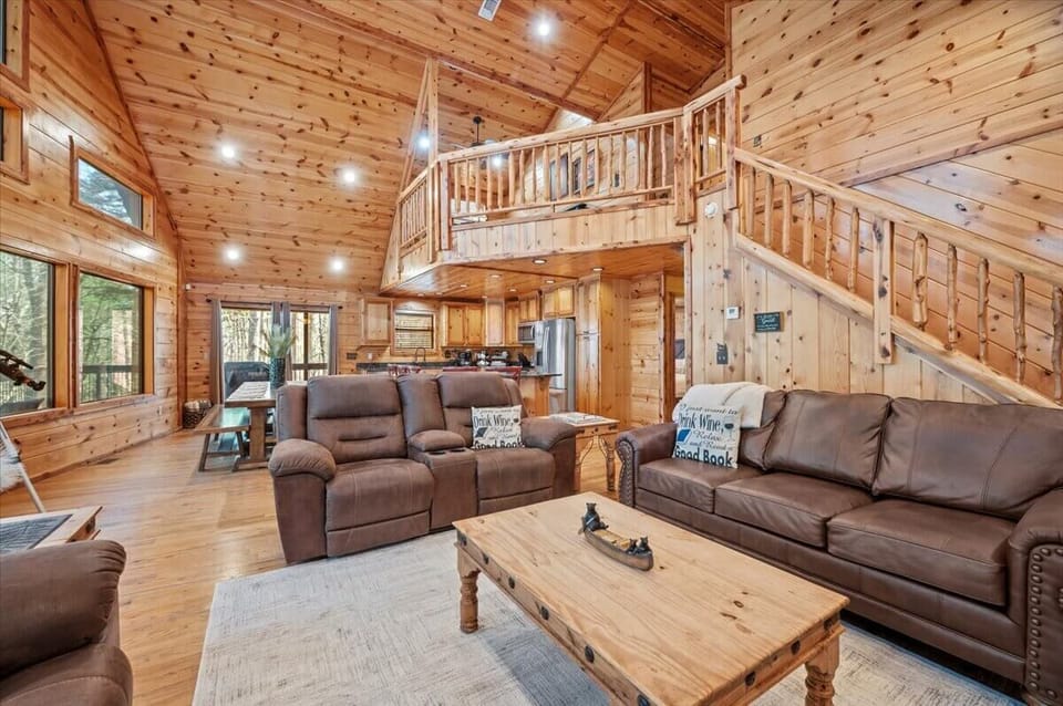 Wood-lined living space with recliners, loft stairs, and forest-view windows.