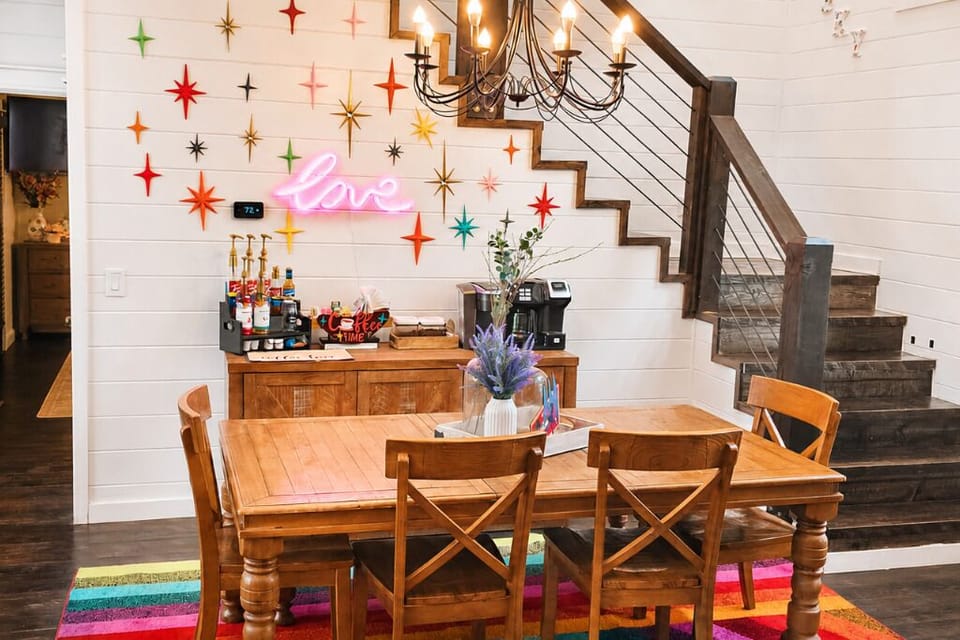 Dining space with farmhouse table, colorful star accents, and neon “love” sign.