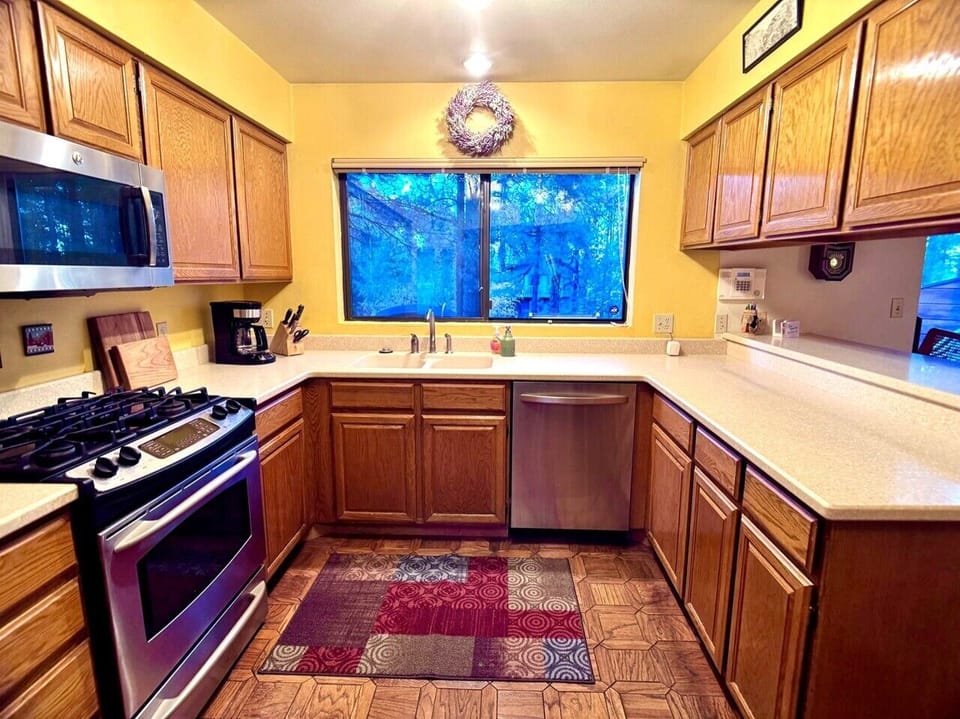 Bright kitchen with dishwasher, sink, coffee station, and wooded views from the window.