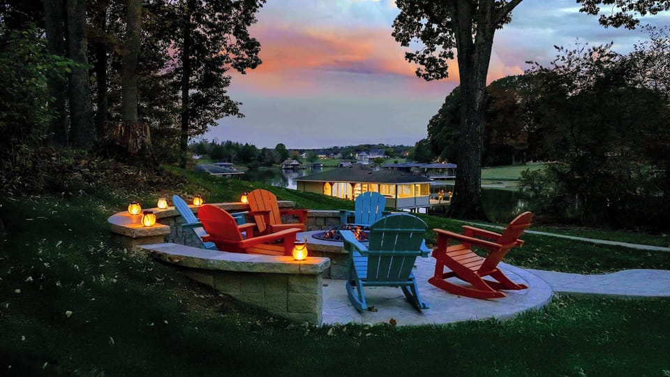 Lit fire-pit circle tucked into the hillside with Adirondacks in bright, joyful lagoons of color — sunset here feels like a ritual.