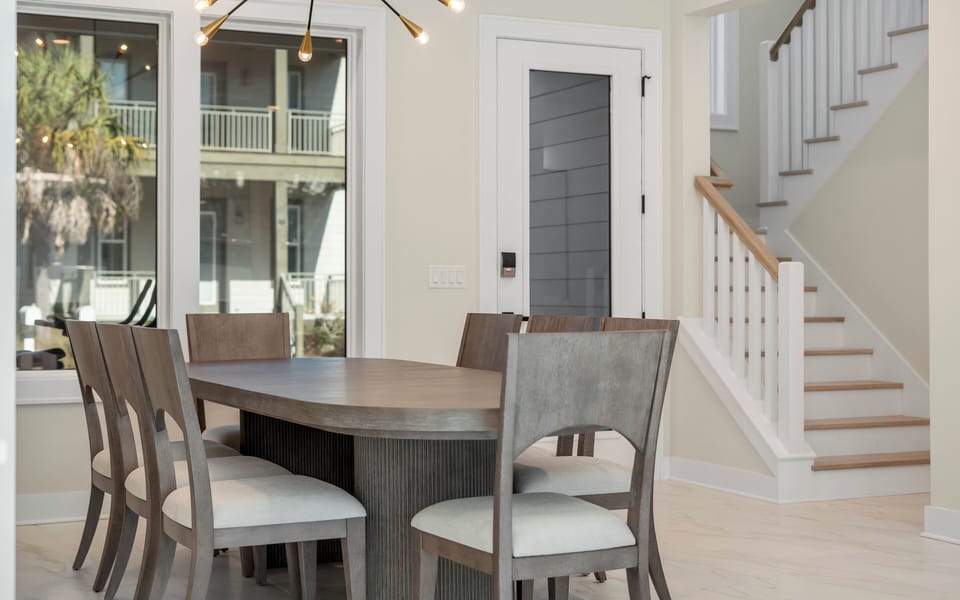 Gather around this elegant dining table for memorable meals, with natural light streaming through windows and a cozy staircase nearby.