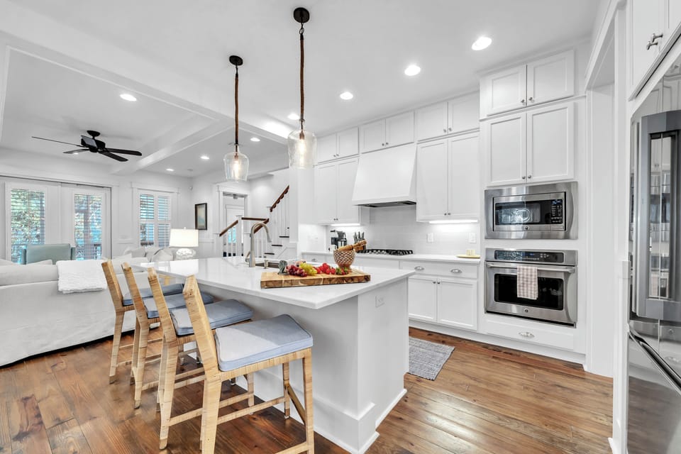 The spacious kitchen flows seamlessly into the living area, featuring gleaming white cabinets, stainless steel appliances, and a breakfast bar for morning coffee.