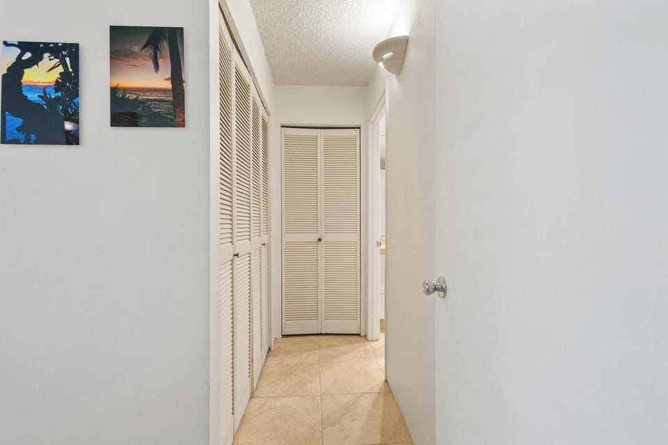 A bright, tiled hallway with ample closet storage connects your living spaces, accented by coastal artwork that sets a relaxed vacation mood.