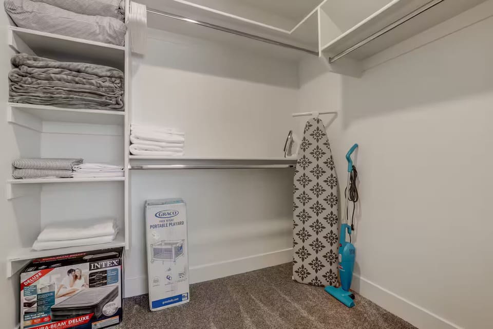 Spacious walk-in closet with extra essentials: inflatable mattresses, ironing board, crib, and vacuum for your convenience.