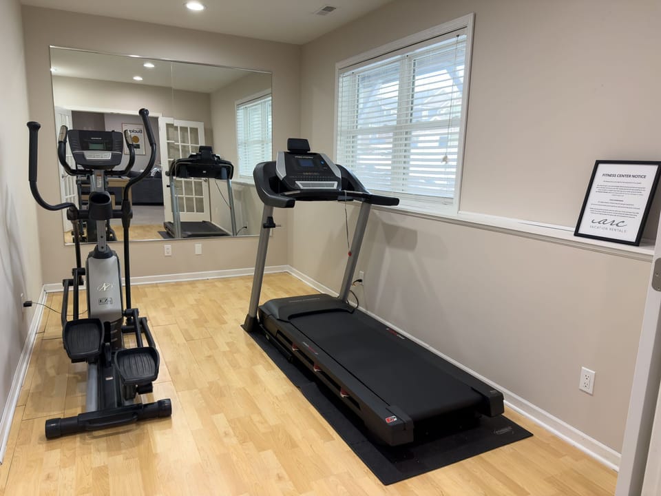 A mirror enhances this multipurpose fitness room, featuring state-of-the-art equipment, providing a motivating environment for workouts with ample natural light.