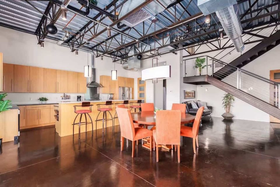 Dining area features a round table with seating for six in plush orange chairs, bathed in natural light with city views from the adjacent patio.
