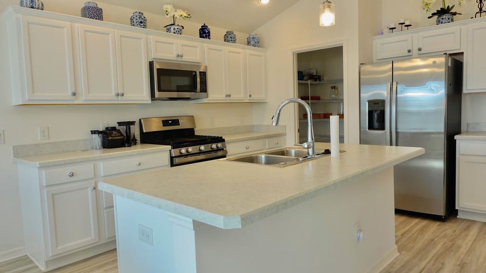 Your bright, modern kitchen features pristine white cabinets, sleek stainless steel appliances, and a spacious island perfect for morning coffee or meal prep.