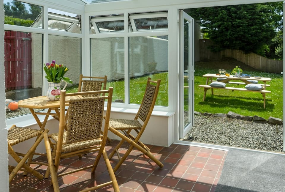 Conservatory with table and four chairs and double doors open to the garden with picnic bench