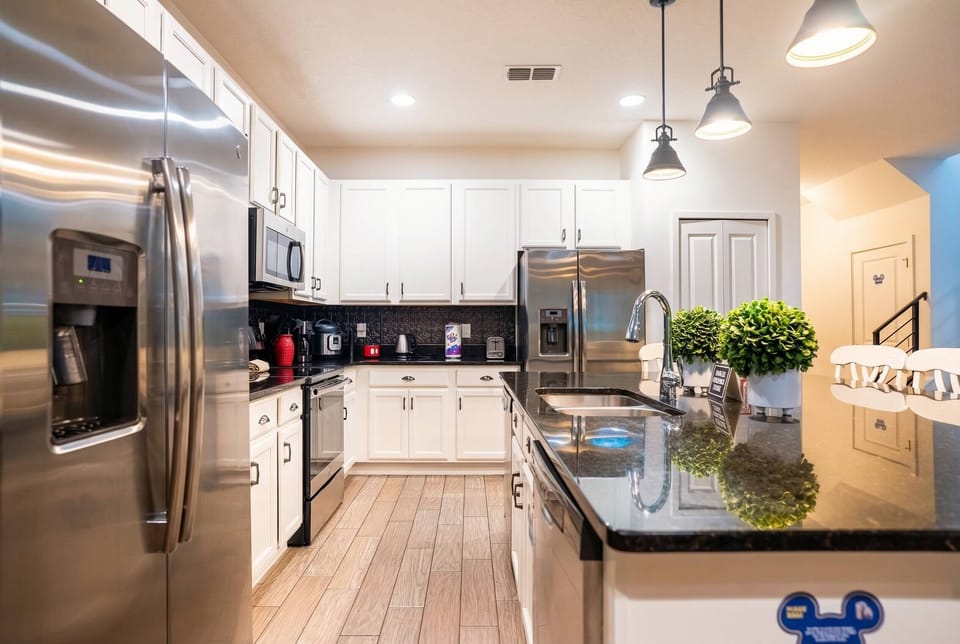 Prepare meals in a bright, fully equipped kitchen with white cabinets, stainless steel appliances, black counters, and pendant lighting. The island with bar seating creates a practical spot for breakfast, snacks, and family time.
