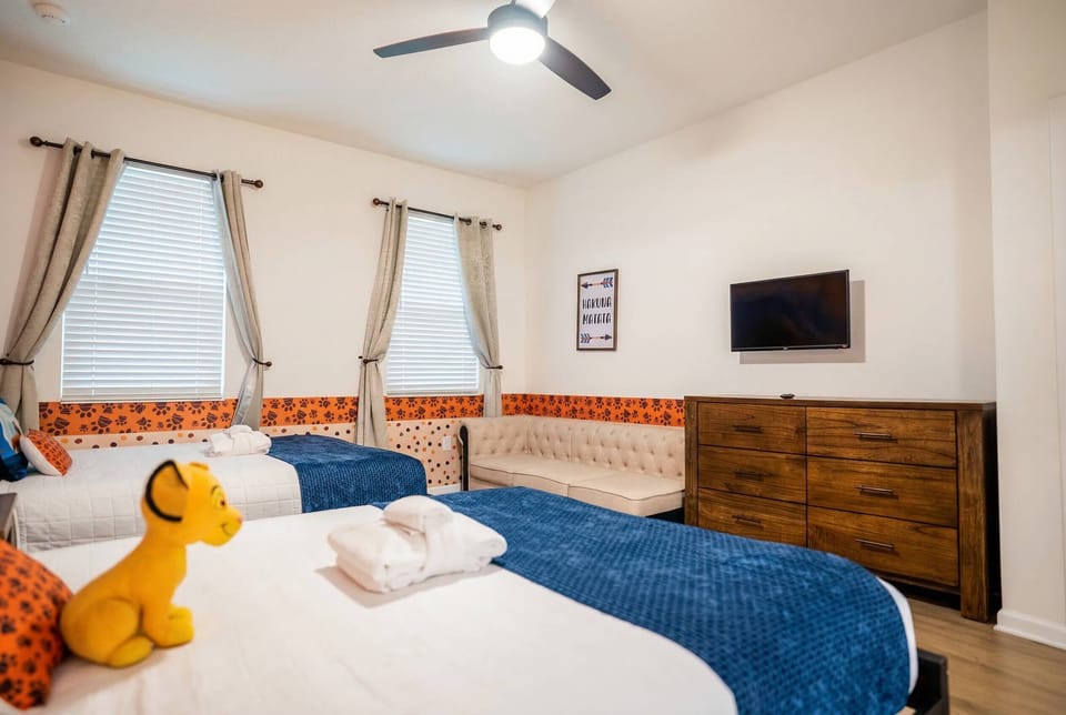 Rest in a bright safari-themed bedroom with two cozy beds, blue accents, soft curtains, a wall-mounted TV, and a comfortable seating area. Playful details and warm wood floors create a relaxing space for family vacation.