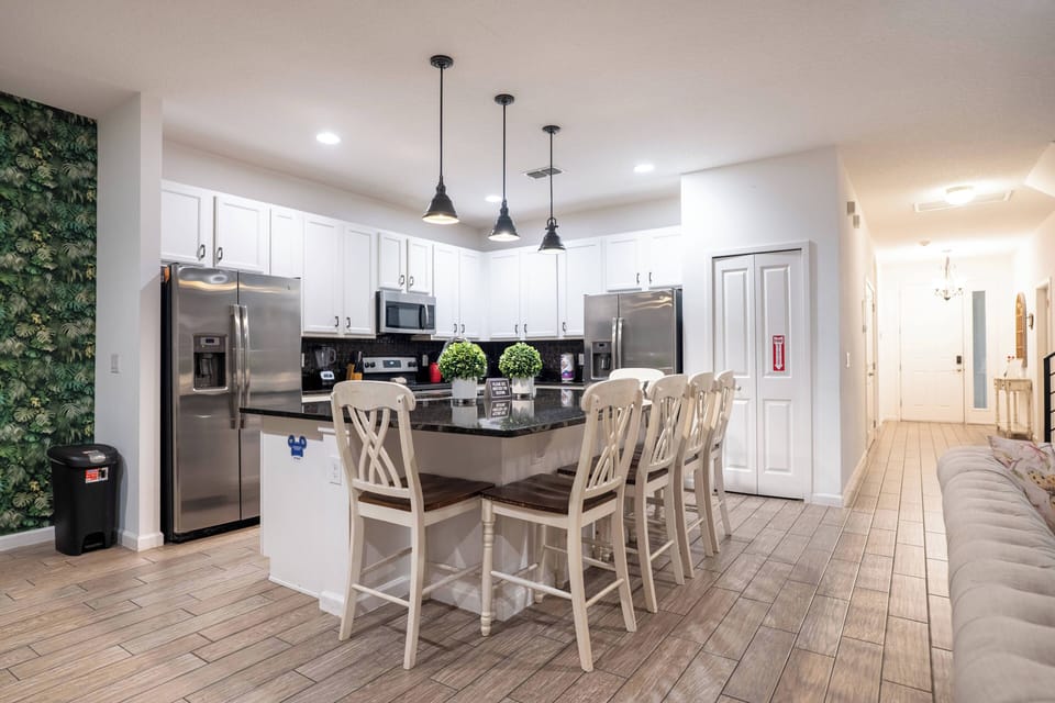 Prepare meals in a bright, fully equipped kitchen with white cabinets, stainless steel appliances, black counters, and pendant lighting. The island with bar seating creates a practical spot for breakfast, snacks, and family time.