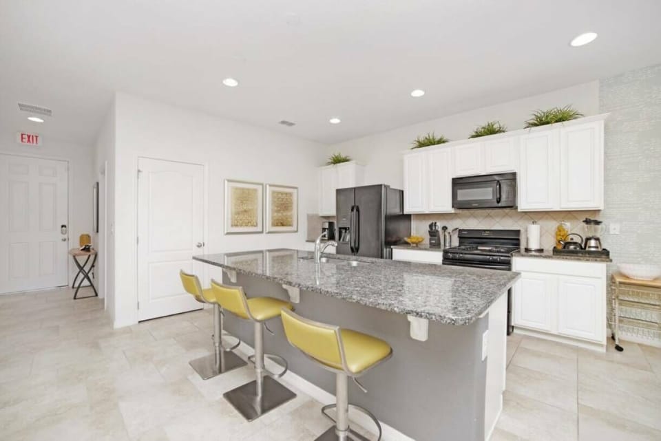 Bright and functional, this kitchen features sleek white cabinetry paired with a striking granite island, perfect for casual dining. The cheerful yellow bar stools add a pop of color, inviting guests to gather and enjoy the space.