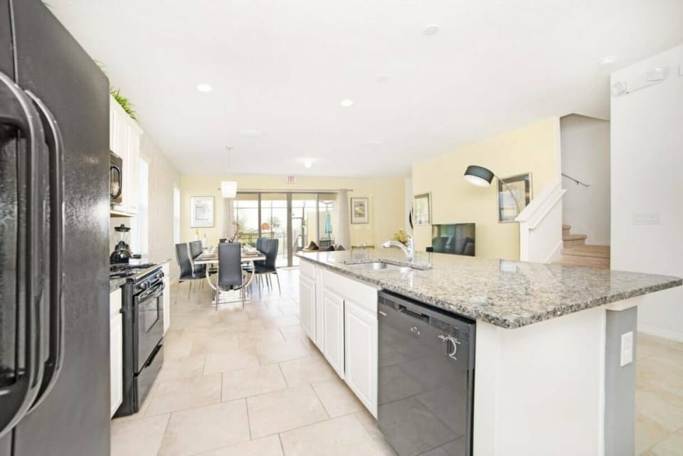Welcome to a bright kitchen with a spacious island and sleek granite countertops, ideal for meal prep or casual dining. Modern black appliances enhance the light cabinetry, and large windows bathe the space in natural light.