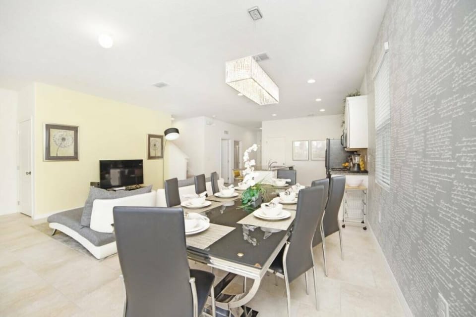 Experience a stylish dining area with a sleek glass table and contemporary gray chairs, perfect for gatherings. The textured accent wall and warm, inviting light fixtures add sophistication and charm to the space.