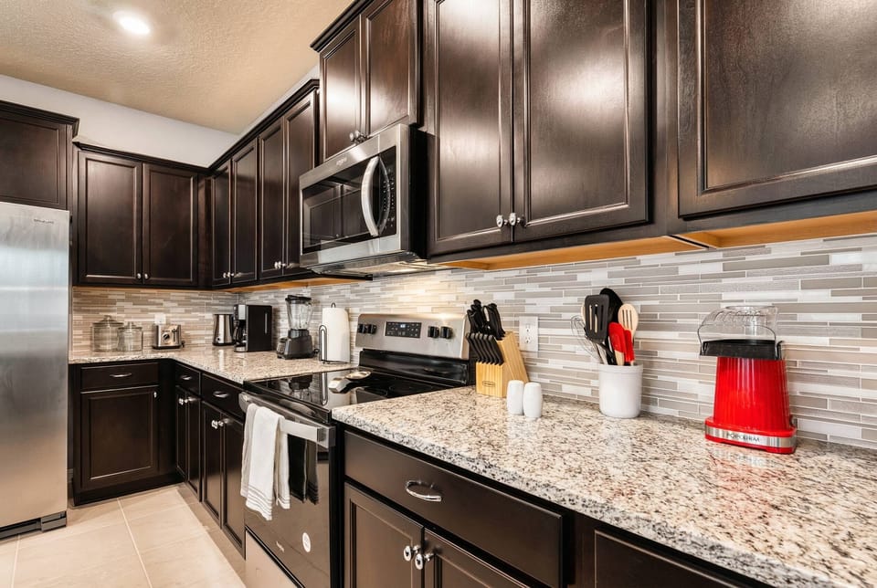 This beautifully designed kitchen features dark cabinetry and sparkling granite countertops, creating a stylish and functional space perfect for effortless meal preparation with modern appliances and a chic backsplash.