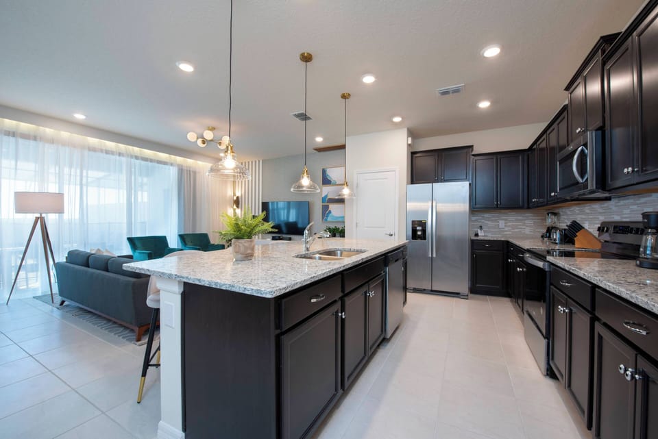 Step into a stylish kitchen featuring rich dark cabinetry and gleaming granite countertops, illuminated by elegant pendant lights. The open layout seamlessly connects to a cozy seating area, perfect for gatherings after meals.