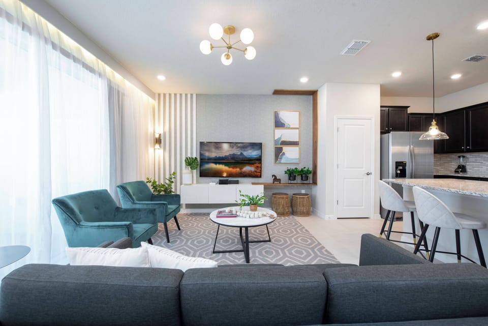 Welcome to a bright living area filled with natural light, showcasing cozy teal chairs and modern decor. The open layout connects effortlessly to a stylish kitchen, perfect for relaxation and entertainment. Enjoy your stay!