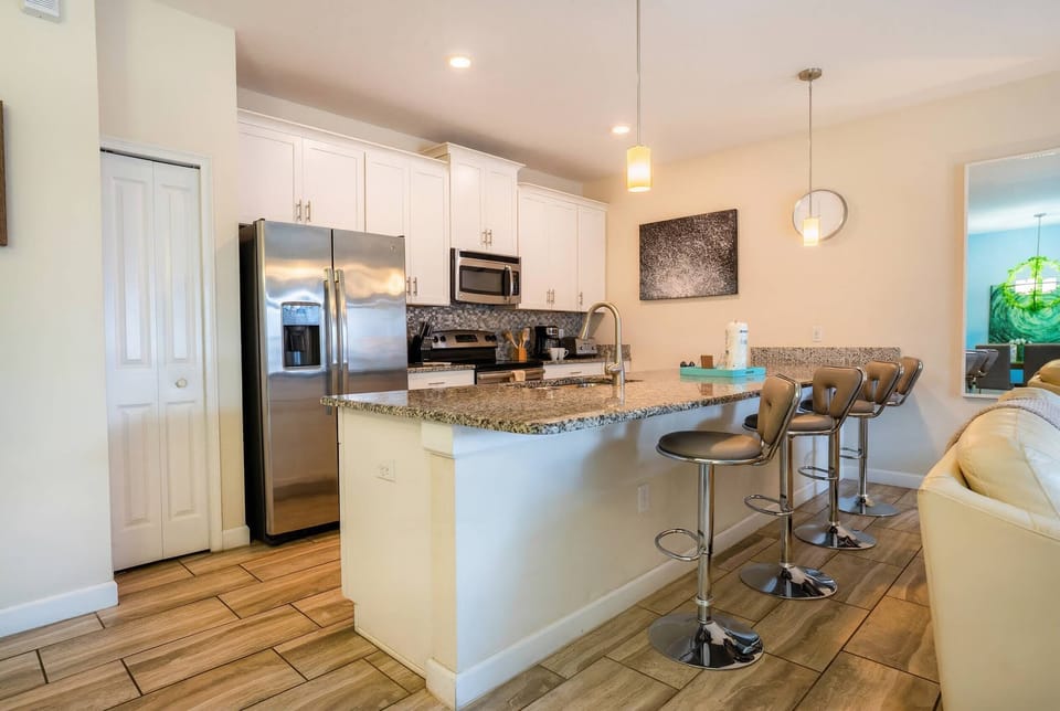 Unwind at the sleek granite island in this modern kitchen, where stainless steel appliances gleam under soft pendant lights. Cozy bar stools invite casual chats or morning coffee, creating a warm, welcoming space for your stay.