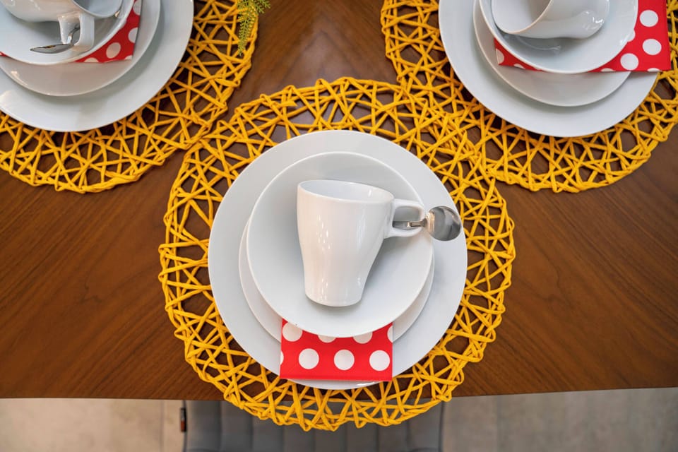 Savor delightful meals at a beautifully arranged table with vibrant yellow placemats and warm wood, complete with polished white dishware and charming red polka-dot napkins, perfect for cozy gatherings.