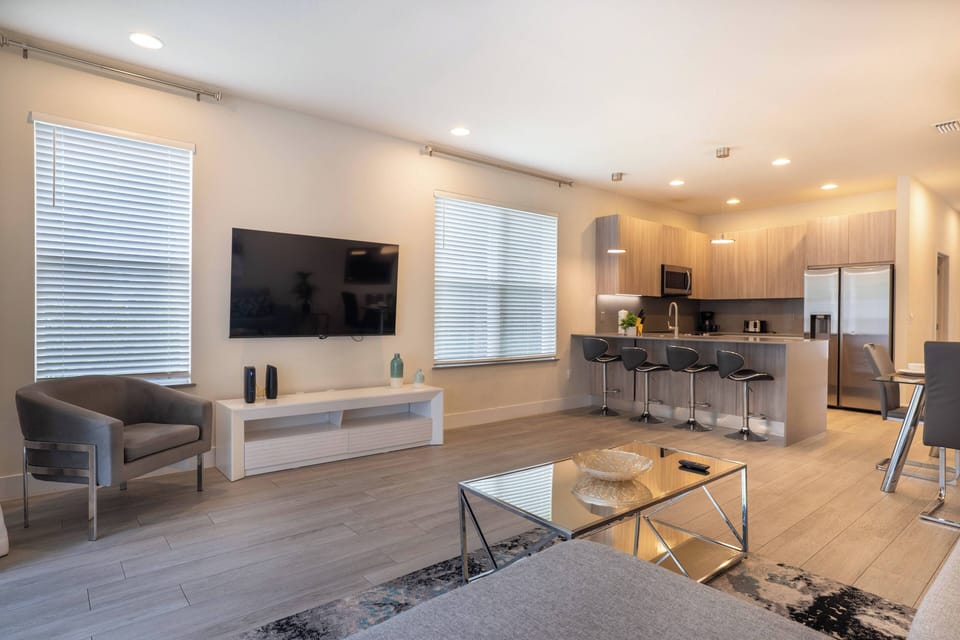 This bright, airy living area combines sleek gray tones and warm wood accents for a cozy, modern feel. Enjoy the modern kitchen with stainless-steel appliances, seamlessly connected to the comfy seating and large windows.