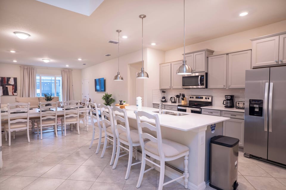 Experience the airy kitchen and dining area featuring sleek stainless steel appliances and a spacious island, ideal for casual meals or morning coffee, all enhanced by modern white cabinetry and warm, inviting lighting.