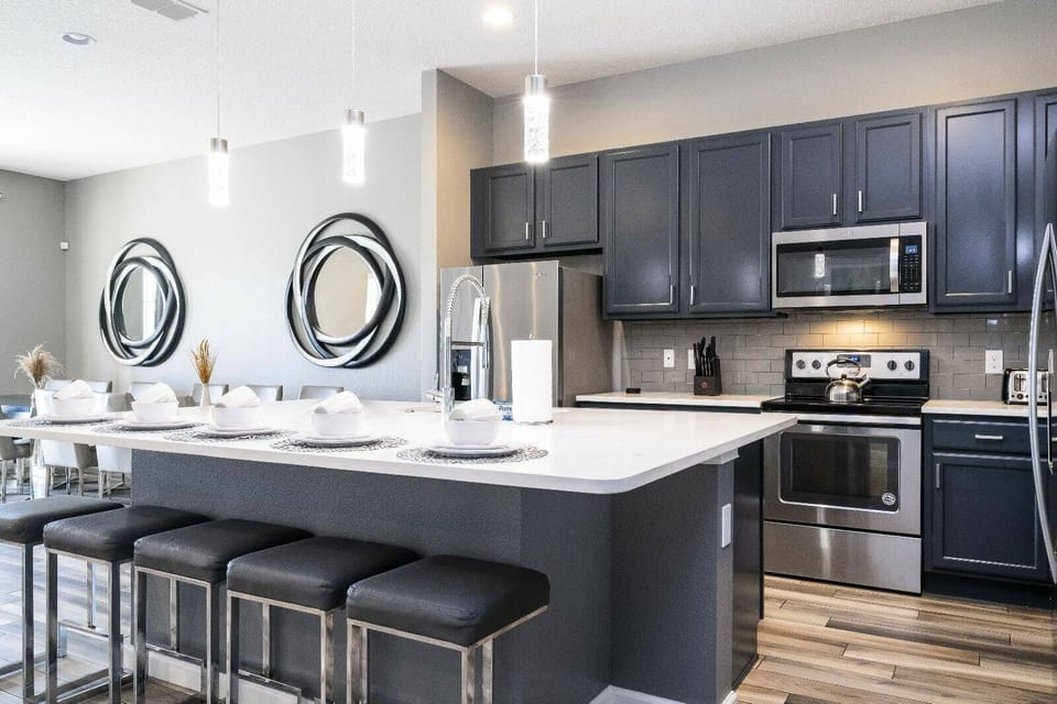 This modern kitchen features stylish navy cabinets and a spacious island with chic bar stools, perfect for casual dining. Bright pendant lights and stainless appliances create a functional and inviting atmosphere for guests.