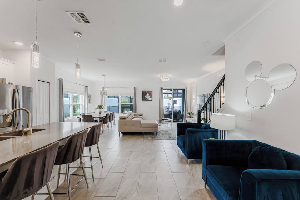 Experience a chic living area with cozy azure seating perfect for relaxation, complemented by elegant pendant lighting over a spacious kitchen island. Large windows fill the space with natural light, showcasing the modern decor.