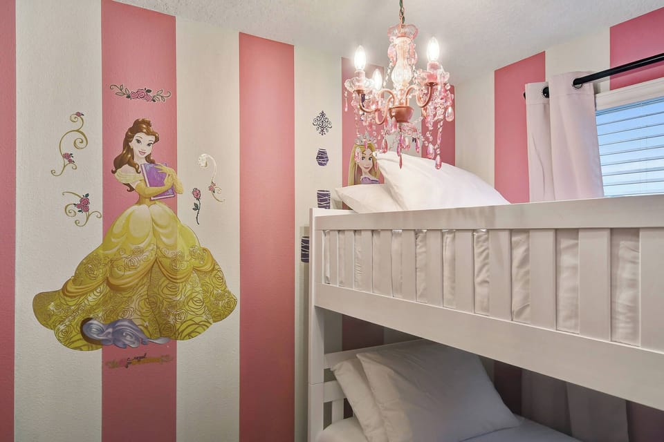 Bright pink striped walls and a charming chandelier create a whimsical atmosphere in this cozy kids' bedroom, featuring a snug bunk bed with fluffy pillows and a delightful princess mural for a fun and inviting stay.
