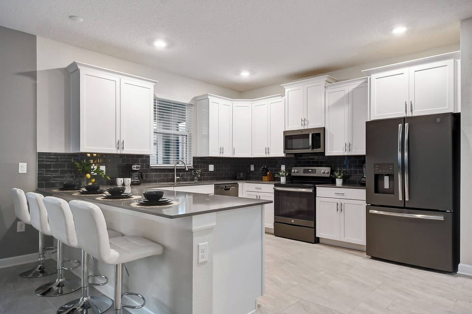 Experience a culinary haven with sleek white cabinetry and a striking dark backsplash, creating a fresh, polished atmosphere. The spacious island with stylish bar stools is perfect for casual gatherings and entertaining.
