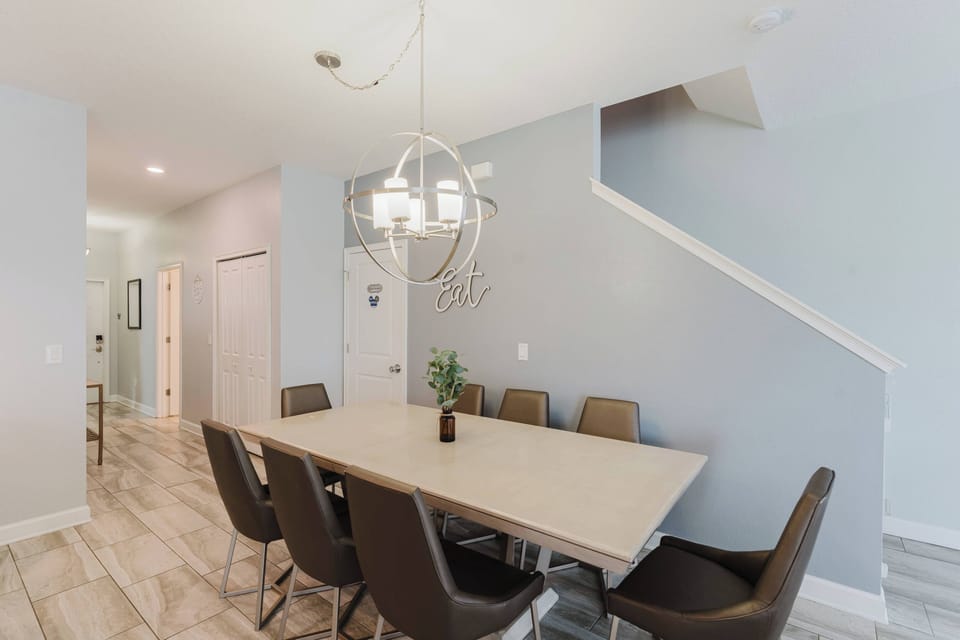 This stylish dining area boasts a sleek light-colored table and contemporary chairs, ideal for family meals or game nights. A modern chandelier adds a warm glow, creating an inviting atmosphere against the soft, muted walls.