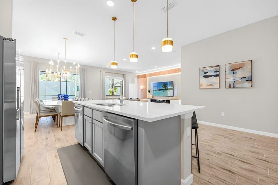 Welcome to this bright kitchen with sleek gray cabinets and a spacious island ideal for casual dining and meal prep. The warm wooden flooring and golden pendant lights create a welcoming atmosphere that flows seamlessly into the.