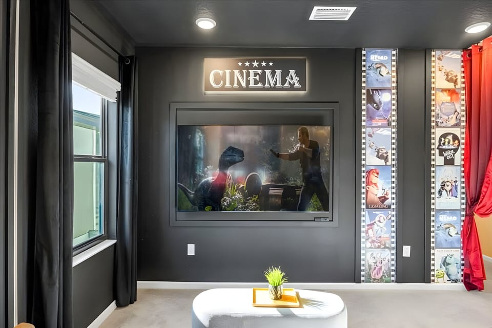 Enter your private cinema with plush black walls, where a large screen awaits amid colorful film decor and rich red drapery, setting the perfect cozy atmosphere for unforgettable movie nights and relaxation.
