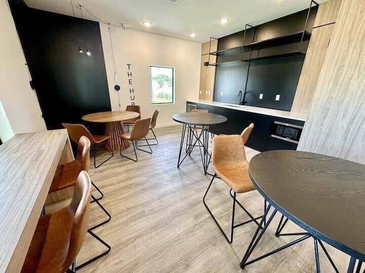Experience a contemporary dining space with light wood flooring and sleek black accents. Relax in tan leather chairs around modern round tables, perfect for stylish dining and engaging conversations.