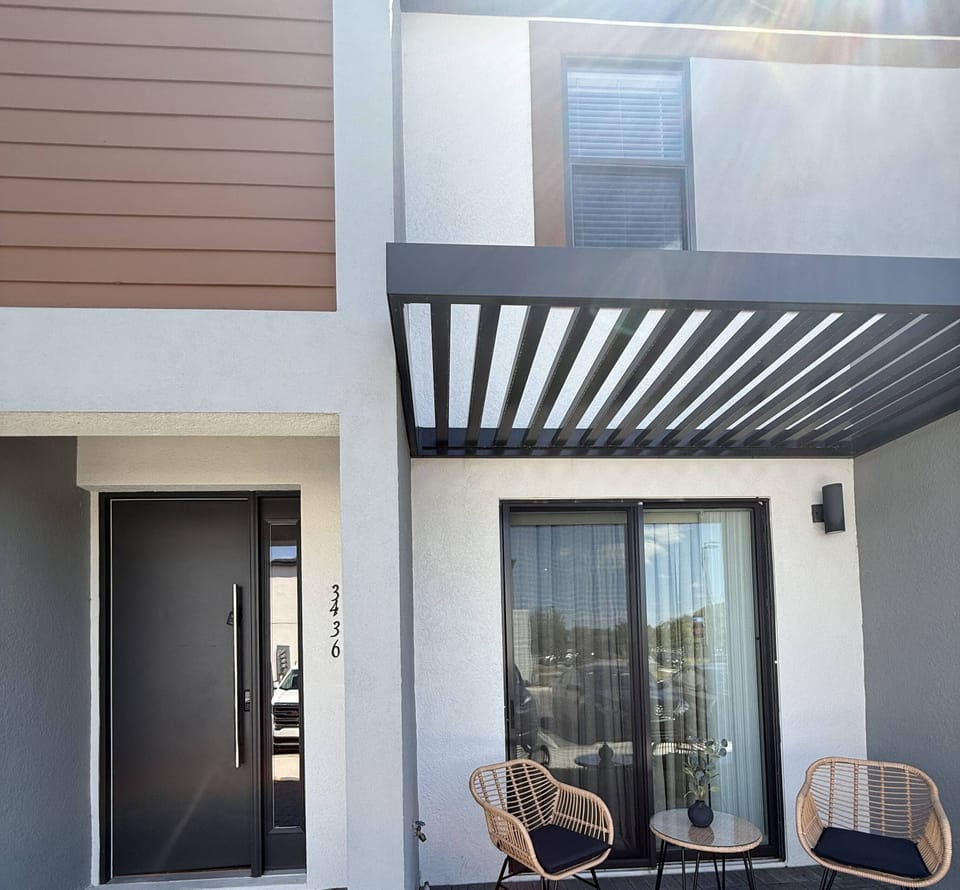 Step into a welcoming entrance with a sleek black door and modern outdoor seating, perfect for morning coffee. The textured stone patio complements the contemporary design, creating a stylish entryway to your next adventure.