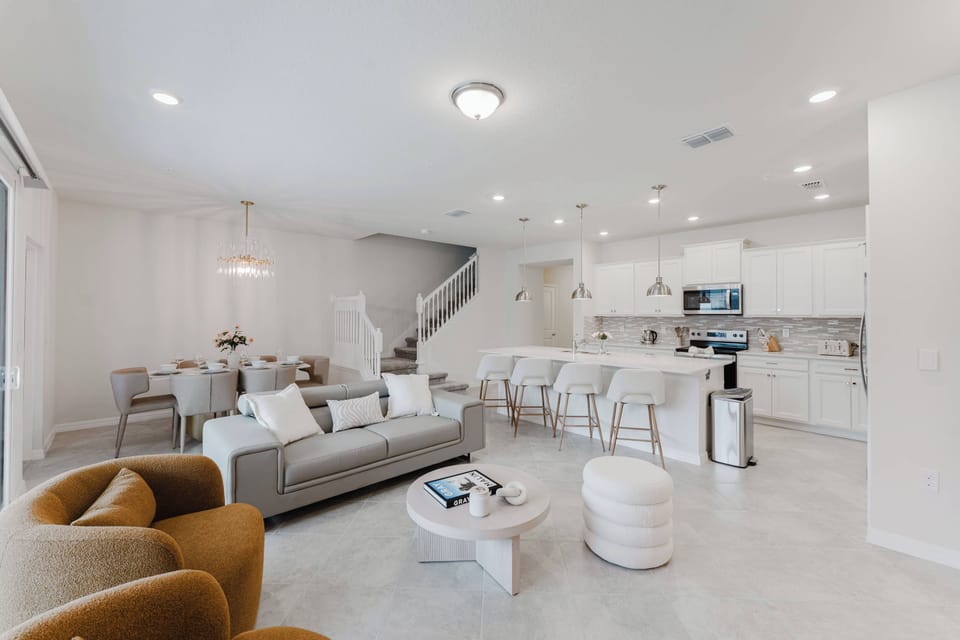 Step into a bright, airy living area where soft gray furnishings harmonize with warm wooden accents. The open layout seamlessly connects the cozy seating with a stylish kitchen, inviting you to relax or whip up a delicious meal.