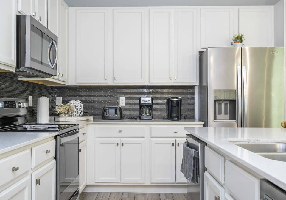 Welcome to a bright kitchen with crisp white cabinetry and sleek stainless-steel appliances, inspiring your culinary creativity. The modern gray backsplash enhances the ample counter space, ideal for all your cooking needs.